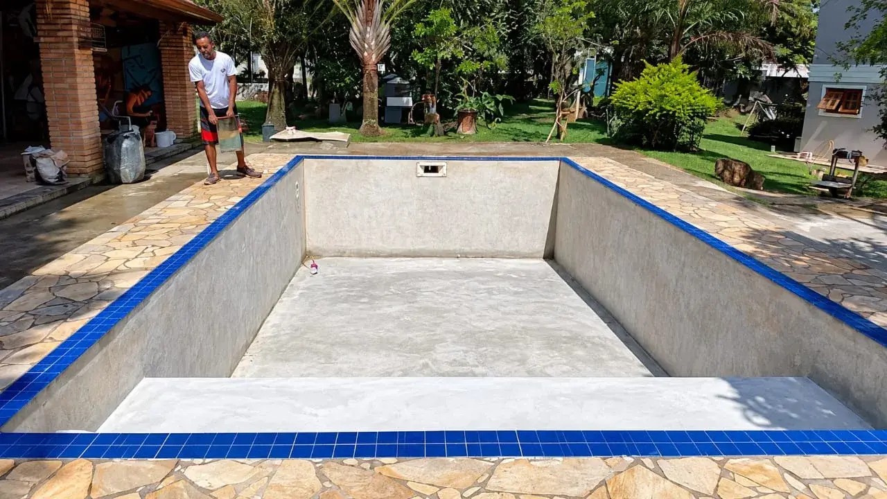 Piscina de alvenaria vazia durante a reforma, com paredes preparadas e faixa de pastilha azul na borda