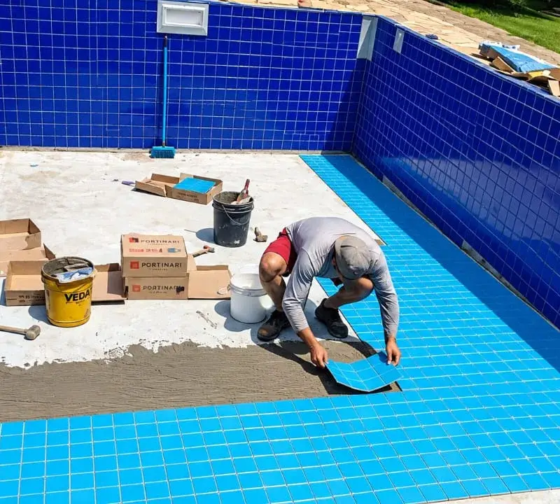 Profissional da Marks assentando pastilha azul no fundo de uma piscina em reforma, no Bairro do Portão, em Atibaia