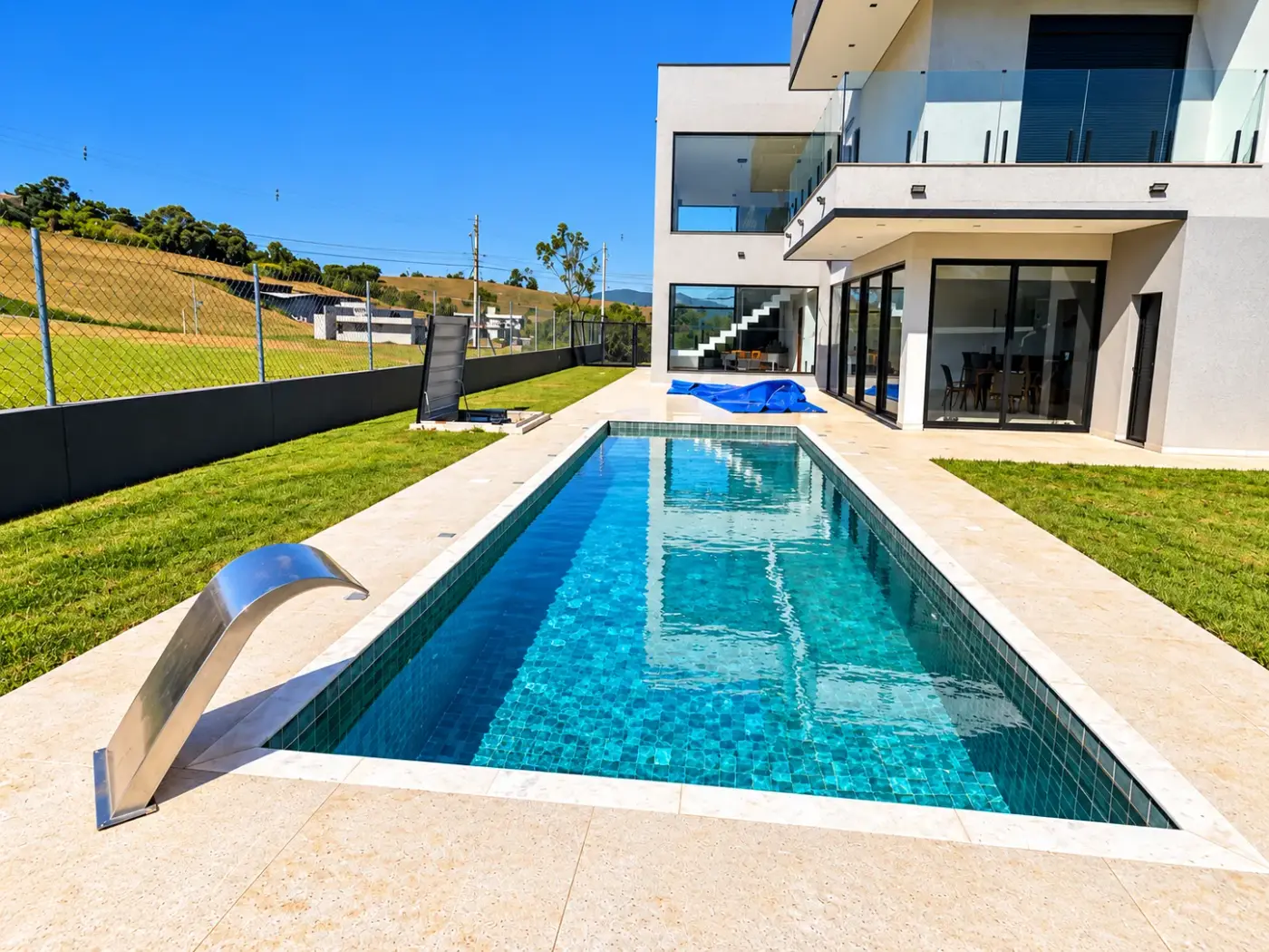 Piscina de alvenaria com cascata de inox, ao lado de uma casa moderna de dois andares, em Joanópolis