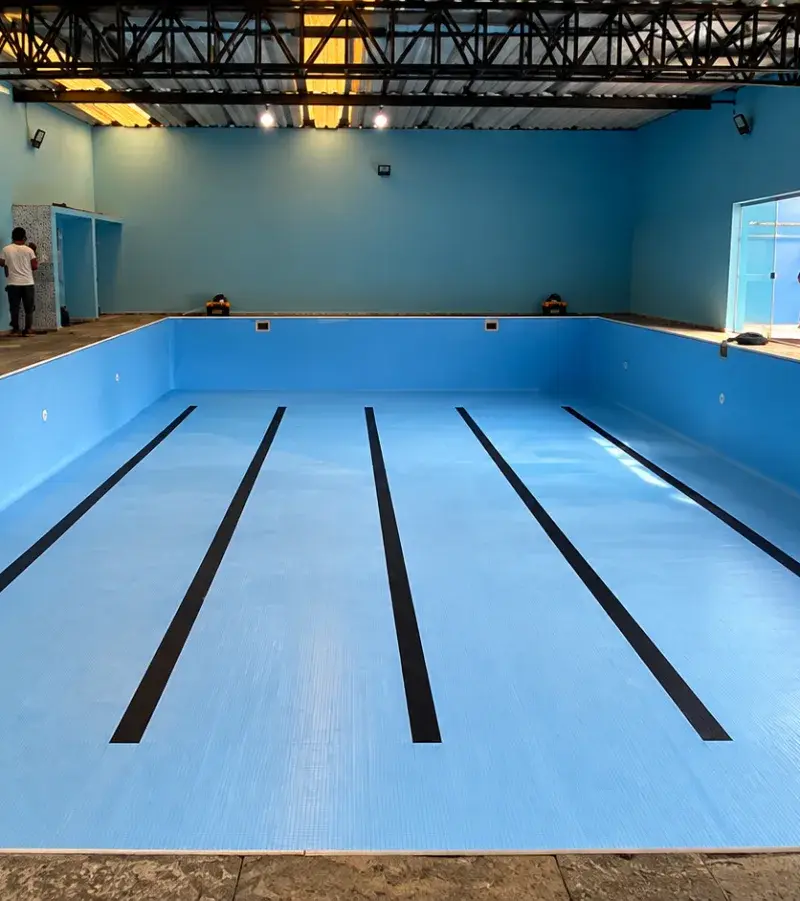Piscina semi-olímpica coberta de academia com vinil azul novo e raias pretas pintadas no fundo, em São Bernardo do Campo