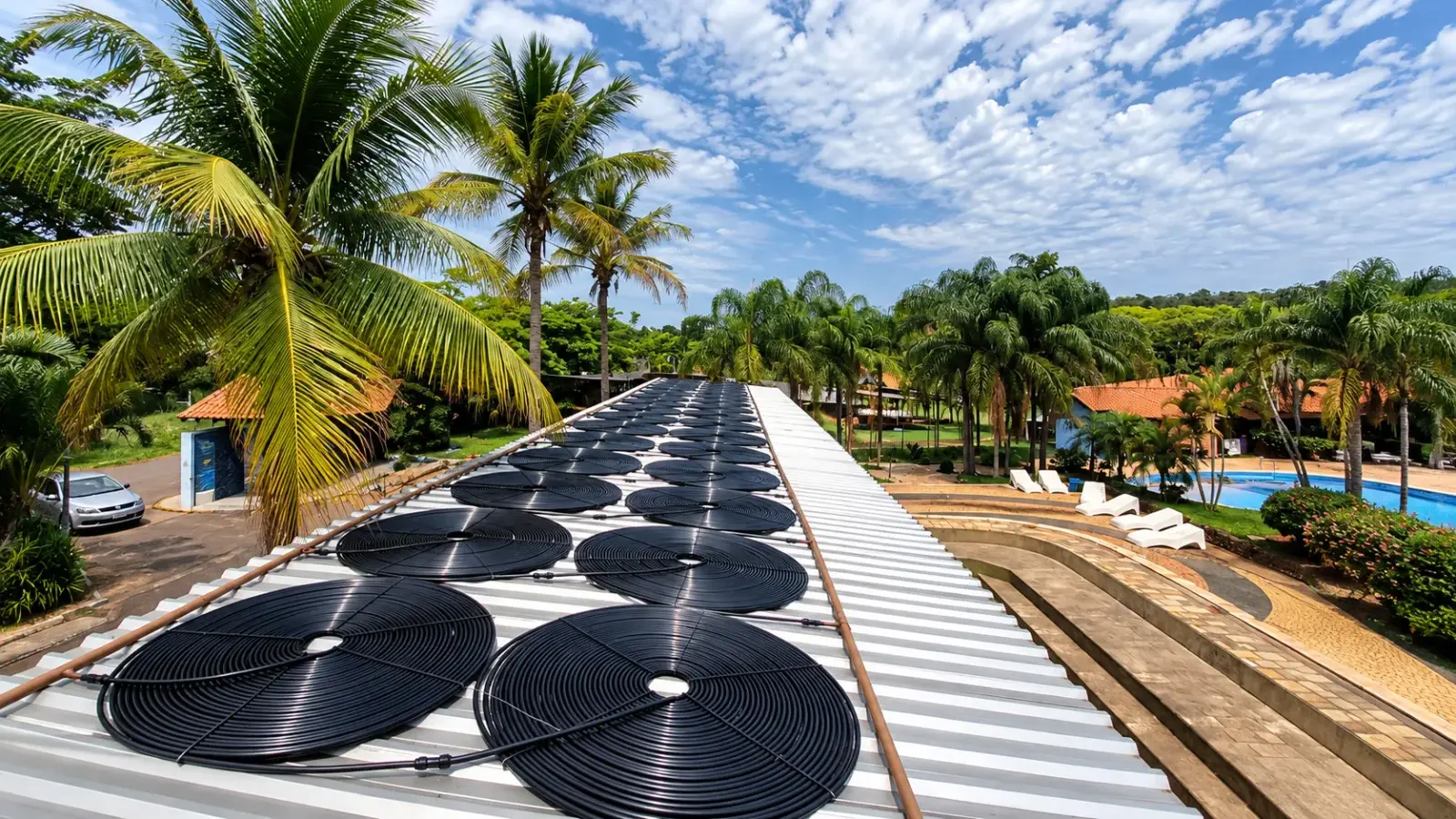 Coletores solares pretos sobre um telhado, ao lado de piscinas e coqueiros, em obra de aquecimento da Marks Piscinas num condomínio em Santos