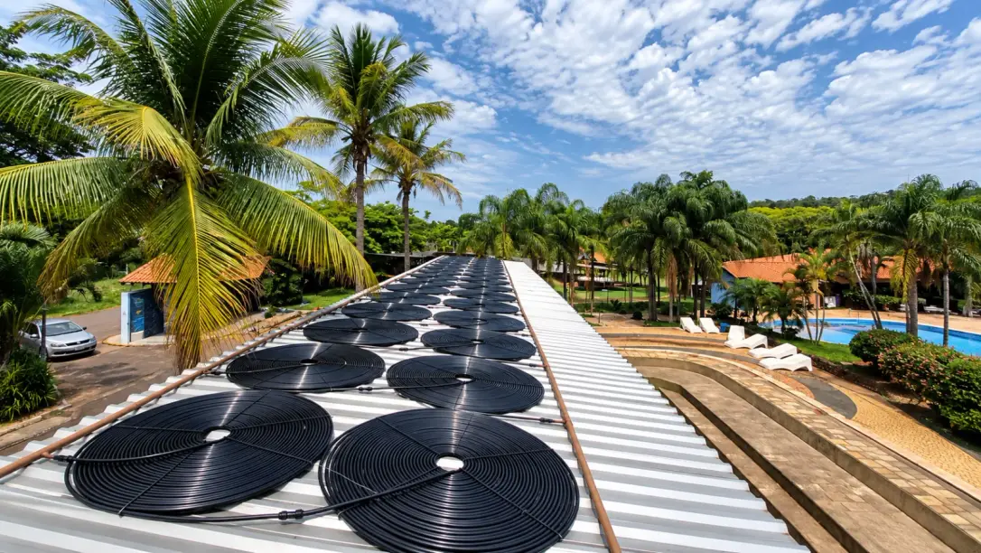 Coletores solares pretos sobre um telhado, ao lado das piscinas de um condomínio em Santos