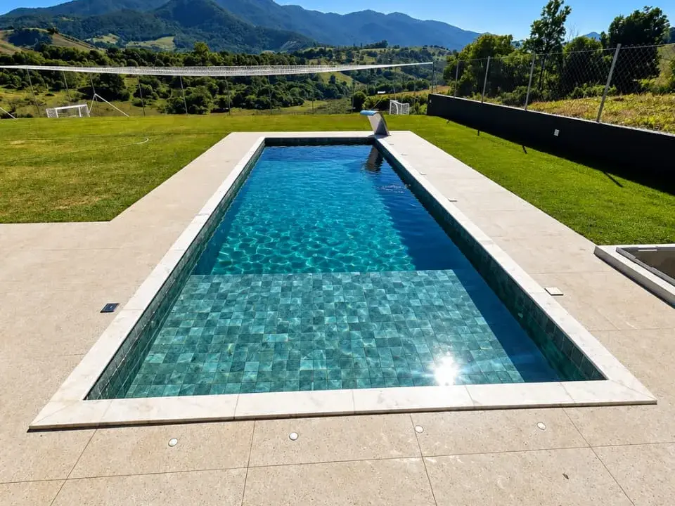 Piscina de alvenaria retangular com pastilhas verdes e borda clara, com montanhas ao fundo, em Joanópolis