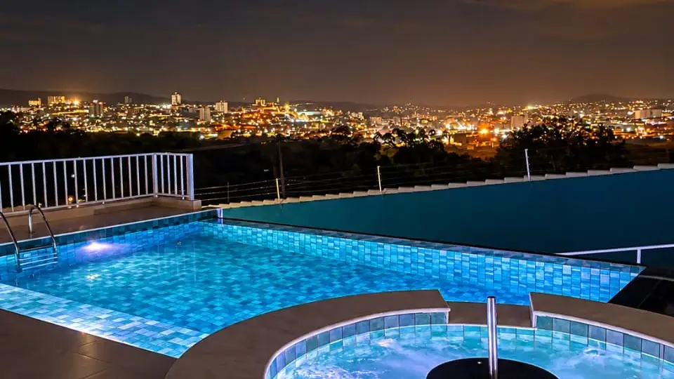 Spa redondo com hidromassagem iluminado ao lado da piscina, com vista noturna da cidade, em obra da Marks Piscinas