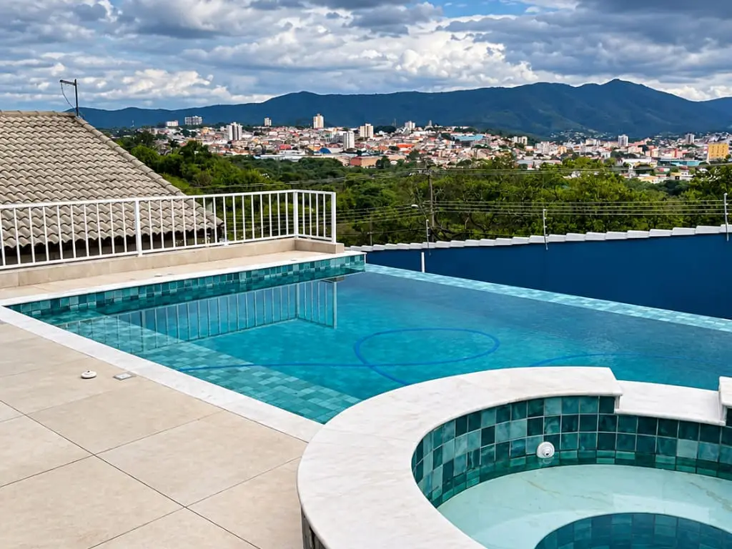 Piscina com spa redondo elevado e borda clara, com vista para a cidade de Atibaia e as montanhas ao fundo