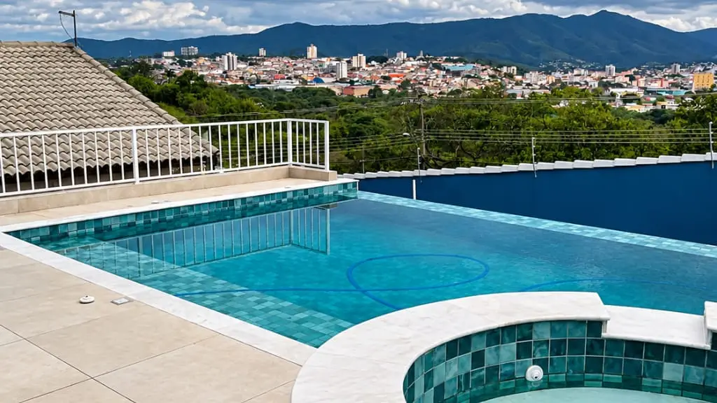 Piscina com spa redondo elevado e borda clara, com vista para a cidade de Atibaia e as montanhas ao fundo, em obra da Marks Piscinas