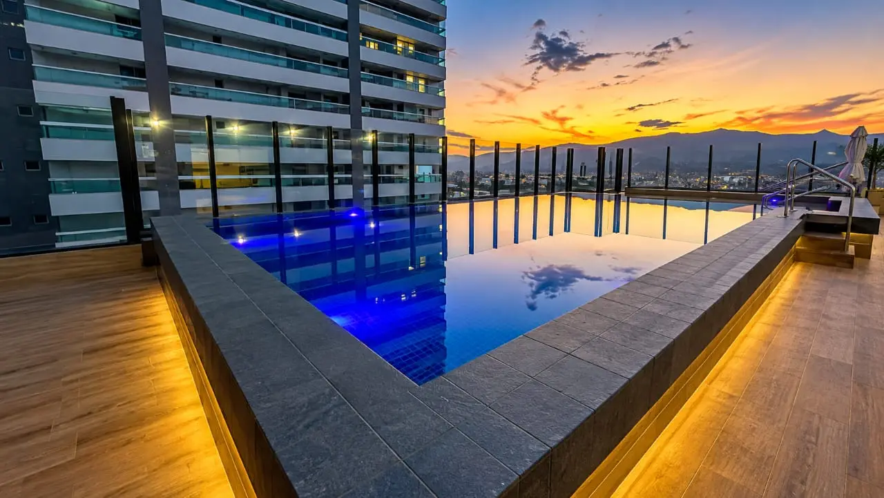Piscina de alvenaria com deck de madeira e luz embutida na borda, num condomínio em Praia Grande
