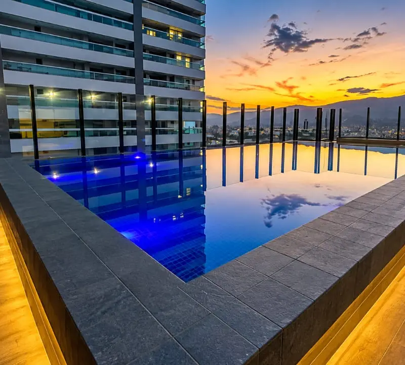 Piscina de alvenaria com deck de madeira e luz embutida na borda, num condomínio em Praia Grande