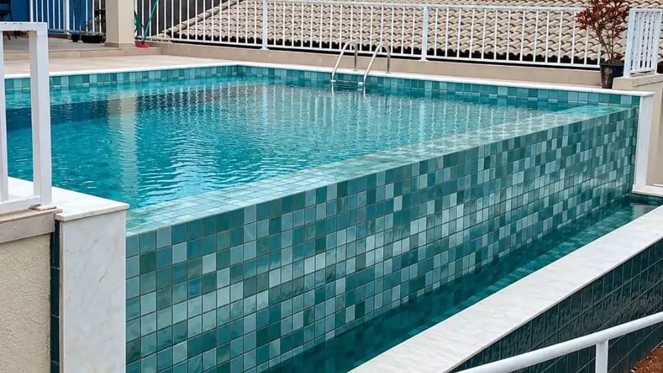 Piscina de alvenaria elevada com revestimento de pastilha em tons de verde e azul, em obra da Marks Piscinas em Atibaia