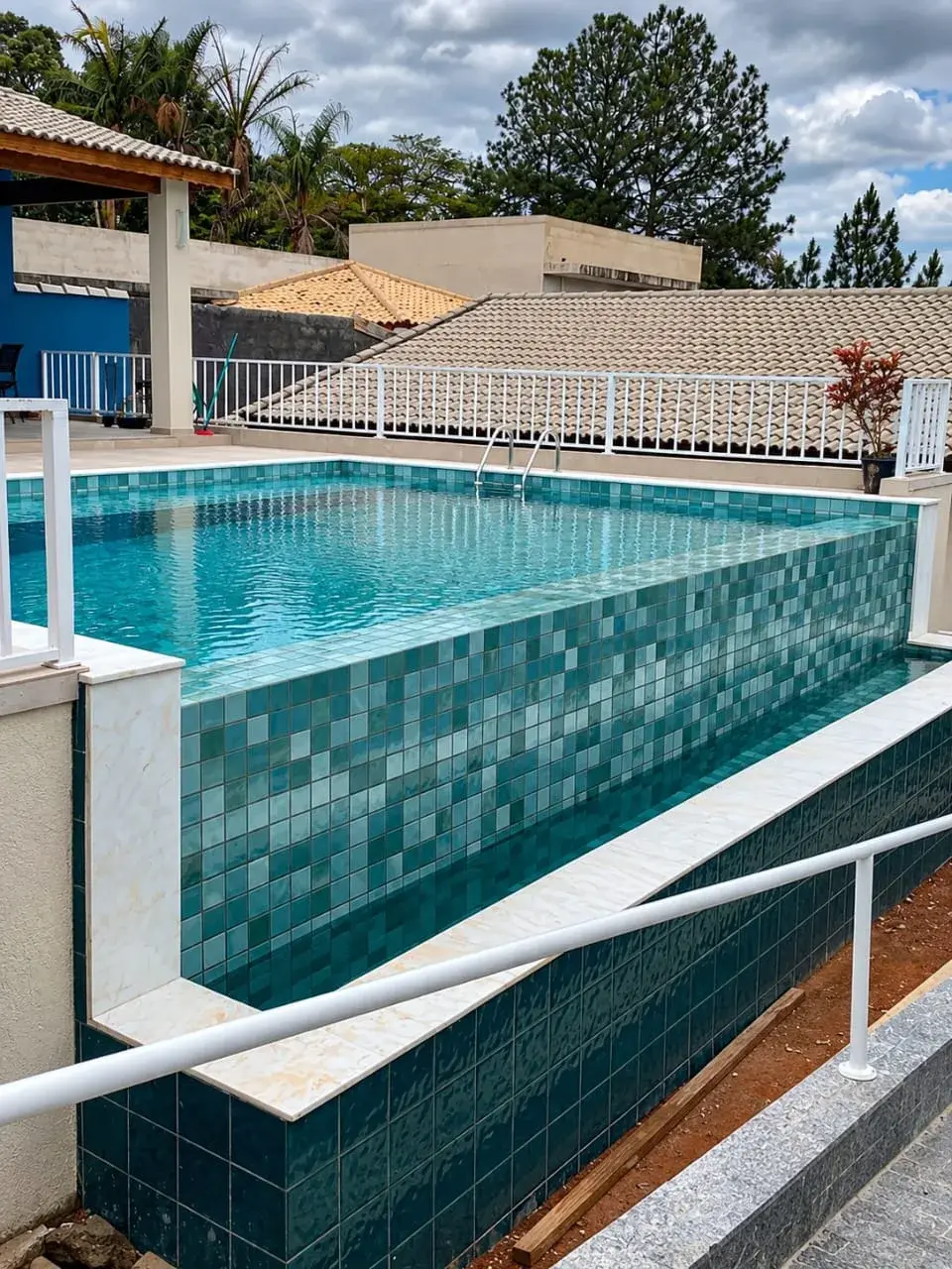 Piscina de alvenaria elevada com pastilha em tons de verde e azul, no São Felipe, em Atibaia