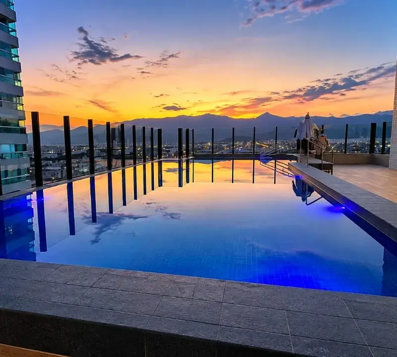 Piscina de alvenaria na cobertura de um condomínio de prédios em Praia Grande, com iluminação azul ao entardecer