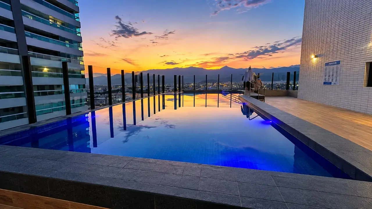 Piscina de alvenaria na cobertura de um condomínio de prédios em Praia Grande, com iluminação azul ao entardecer, em obra da Marks Piscinas