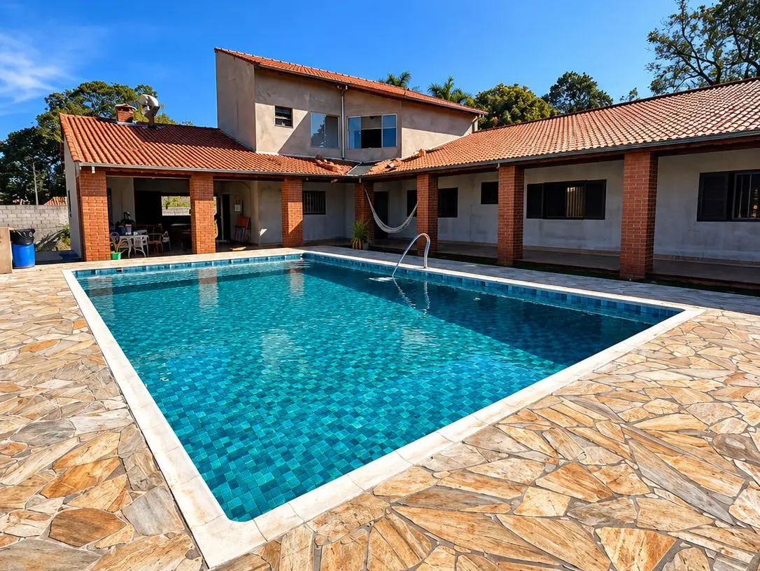 Piscina de vinil retangular azul em chácara, com deck de pedra e casa ao fundo