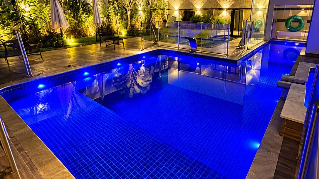 Piscina de vinil iluminada à noite, com a água em tom azul, em obra da Marks Piscinas