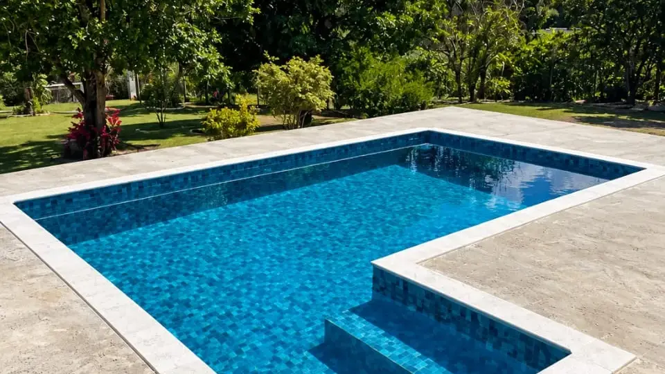Piscina de vinil compacta em formato de L, com degraus e borda de pedra clara, em obra da Marks Piscinas em Salto de Pirapora