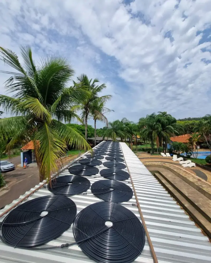 Coletores solares de piscina sobre a cobertura de um condomínio em Santos, com coqueiros ao fundo