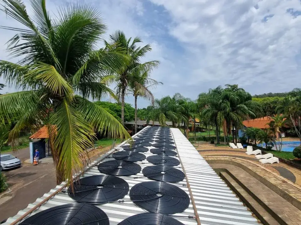Coletores solares de piscina sobre a cobertura de um condomínio, com coqueiros ao fundo
