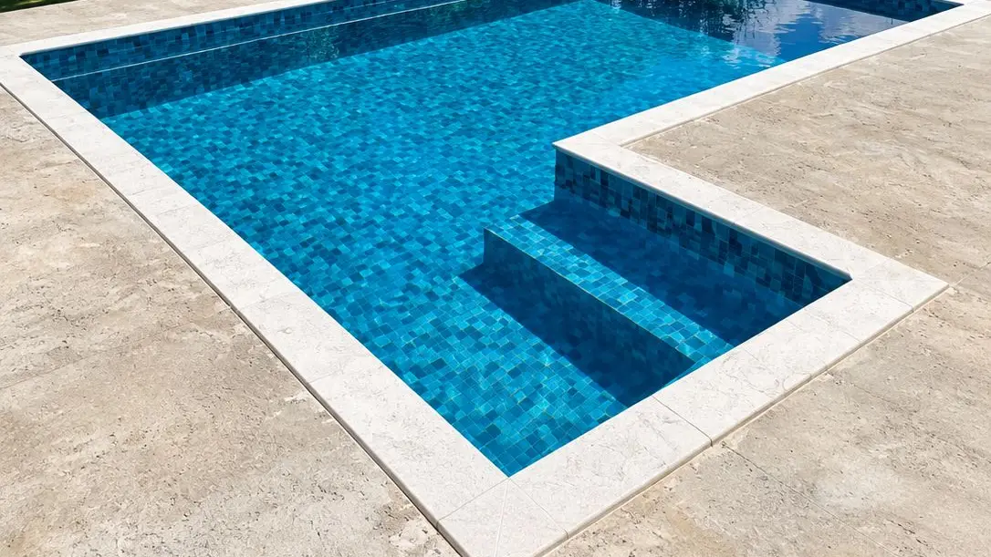 Piscina de vinil azul com degraus em L e borda de pedra clara, em obra da Marks Piscinas