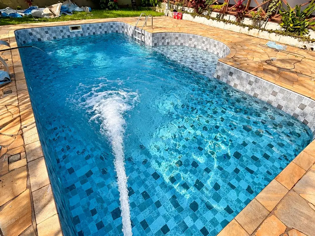 Piscina com vinil novo sendo enchida por uma mangueira, com casa e jardim ao fundo